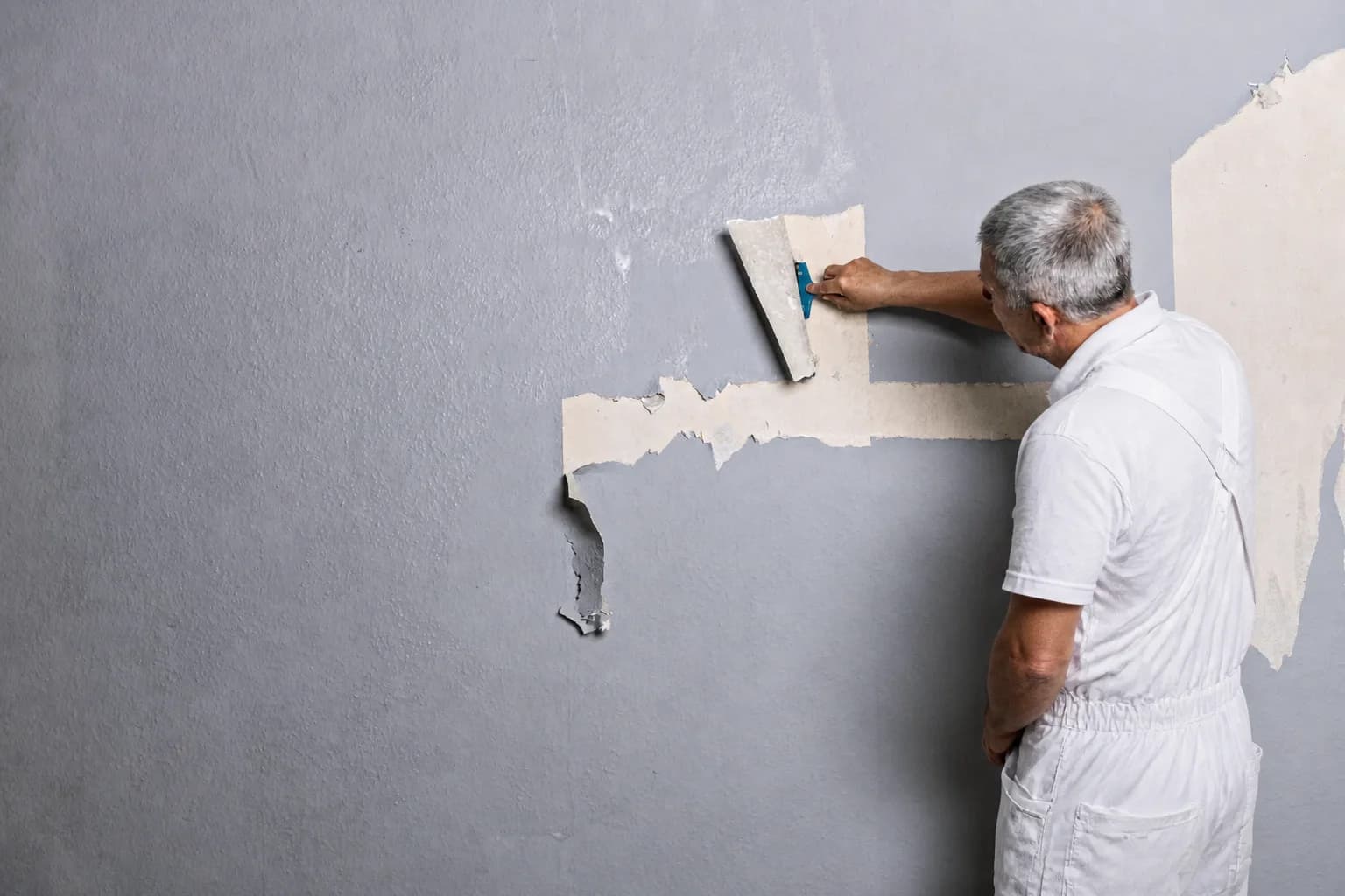 Professionelle Tapetenentfernung, Maler entfernt alte Tapete von Wohnzimmerwand